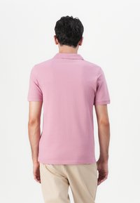 Polo skjorte i lys rosa, korte ermer, myk stoff, ribbet krage, og detaljert søm langs kanten og ermene. Bakfra vises.
