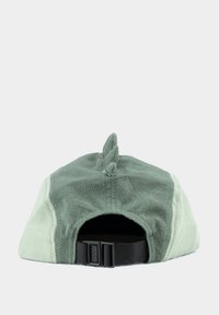 Grüne Mütze mit strukturierter Oberfläche, ausgestattet mit einer Rückenflosse oben und einem verstellbaren schwarzen Riemen auf der Rückseite. Zweifarbige Gestaltung.