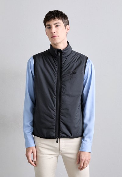 Zwarte geïsoleerde vest met hoge kraag en rits aan de voorkant, gedragen over een lichtblauw shirt. Minimalistisch ontwerp zonder zichtbare patronen of accenten.