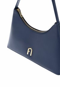 Granatowa skórzana torebka o zaokrąglonym kształcie, złoty zamek błyskawiczny oraz złote logo w kształcie litery z przodu. Gładka tekstura, minimalistyczny design.