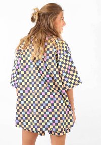 Chemise à manches courtes, oversize, à motif à carreaux avec des couleurs pastel, comprenant des nuances de violet, bleu, jaune et noir.