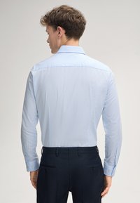 Himmelblaues langärmeliges Hemd mit strukturiertem Muster, geknöpften Manschetten und klassischem Kragen, kombiniert mit dunkelblauen Hosen.