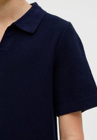 Námornícky polo tričko s krátkym rukávom z textúrovanej pleteniny, s klasickým golierom a rebrovanými manžetami na rukávoch. Obsahuje polovičné gombíky.