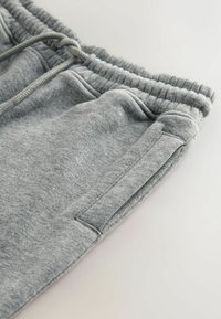 Pantalones de chándal grises hechos de una tela suave. Presentan una cintura elástica con cordón y bolsillos laterales. Textura suave; diseño casual.