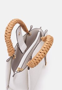 Vit flätad läderhandväska med texturerad yta, bruna flätade handtag, guldhardware och en dragkedja i huvudfacket.