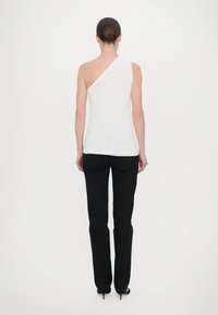 Hvit ribbet topp med én skulderdesign, sammen med svarte slim-fit bukser og høyhælte sandaler. Glatt tekstur, tettsittende silhuett.