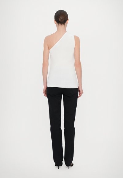 Λευκό ριγέ αμάνικο τοπ με σχέδιο ενός ώμου, συνδυασμένο με μαύρα στενά παντελόνια και ψηλοτάκουνα σανδάλια. Λείο ύφασμα, εφαρμοστό σιλουέτα.