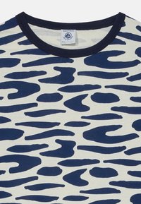 Camiseta de algodón con un patrón abstracto azul marino sobre un fondo crema, con un cuello acanalado azul marino y una etiqueta en el escote.