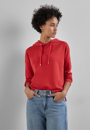 Red hoodie with a front pouch pocket, drawstring hood, and loose fit, paired with high-waisted light blue jeans featuring button details.