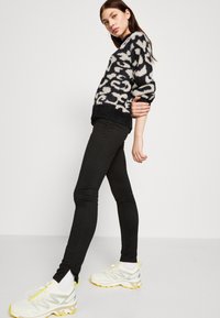 Knitted black and cream patterned sweater with a loose fit, paired with black fitted jeans and white sneakers with yellow accents.