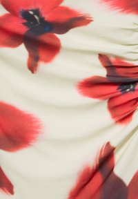 Tissu blanc avec de grands motifs abstraits de fleurs rouges et noires, légèrement froncé sur le côté droit.