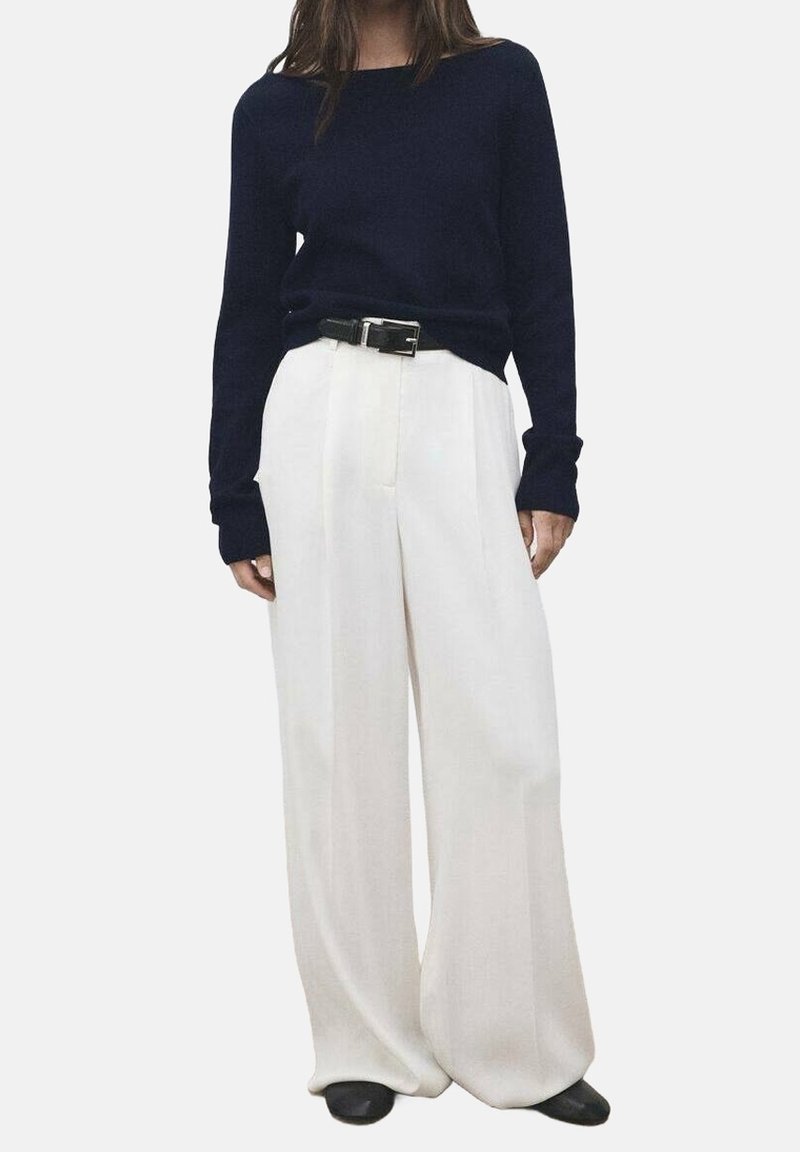 Personne portant un haut à manches longues bleu marine rentré dans un pantalon blanc large taille haute avec une ceinture noire et des chaussures noires.