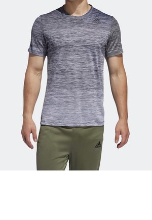 Mężczyzna ubrany w szarą teksturowaną koszulkę z krótkim rękawem Adidas i oliwkowe spodnie Adidas, stojący na jednolitym tle.