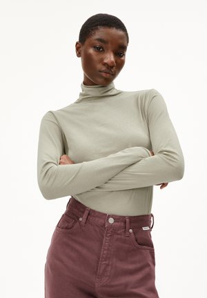 Lichtgrijze longsleeve top met hoge hals; gecombineerd met donkerborstuiten hoge taille broek met voorzakken en metalen hardware accenten.