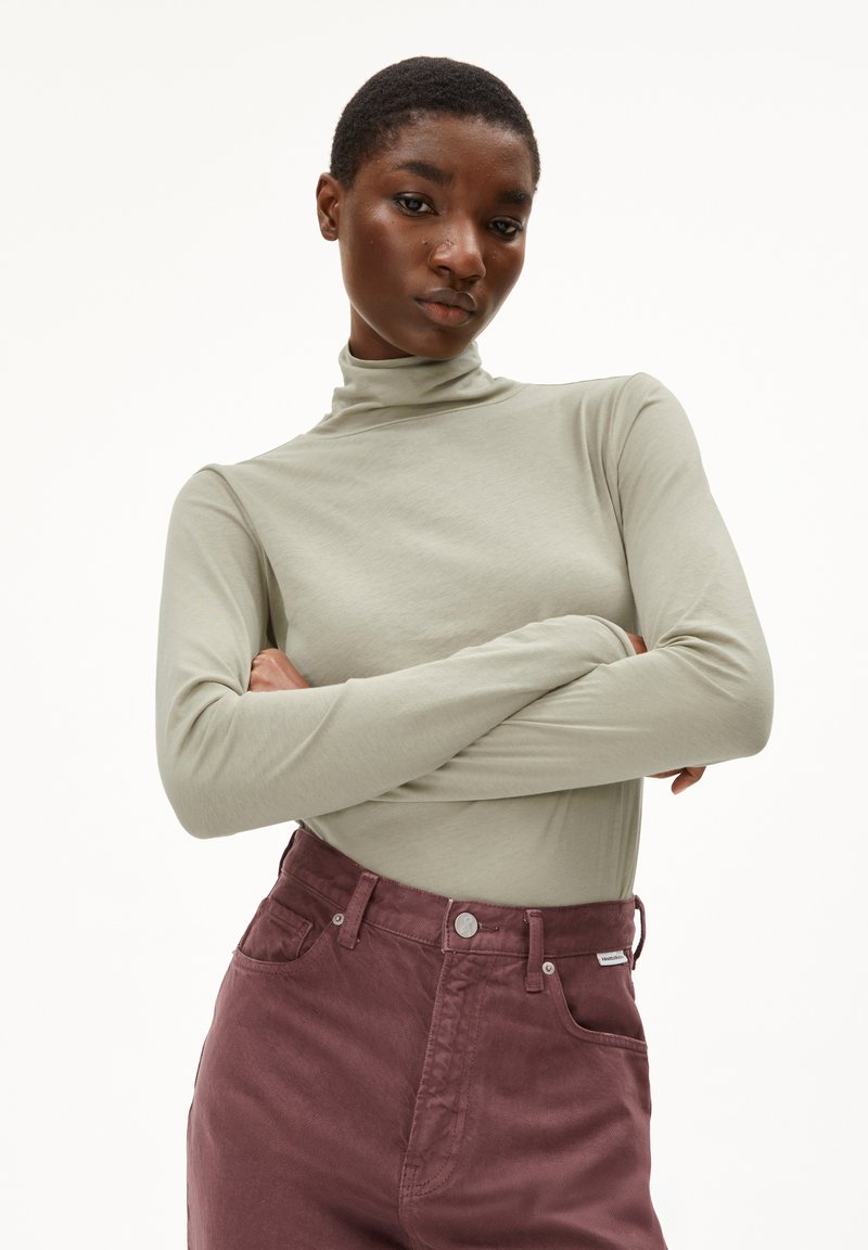 Lichtgrijze longsleeve top met hoge hals; gecombineerd met donkerborstuiten hoge taille broek met voorzakken en metalen hardware accenten.