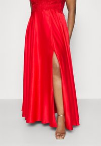 Rotes Satin-Abendkleid mit tailliertem Oberteil, verziert mit Pailletten, und einem schlitz bis zum Oberschenkel sowie einem fließenden, voluminösen Rock.