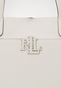 Bijela teksturirana kožna torba s reljefnim srebrnim logotipom "RL" sprijeda, s prošivenim detaljima i čvrstim ručkama.