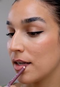 Läpppenna i en dämpad mauve-nyans appliceras på läpparna, med slät hudstruktur och definierad vinge-eyeliner synlig.