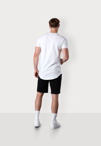 White short-sleeve t-shirt with a rounded hem, paired with black denim shorts. White sneakers and ankle-length white socks.