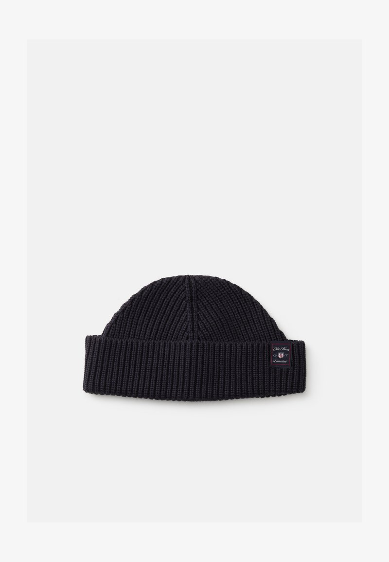 Gebreide beanie in donker marineblauw met een geribbelde textuur en een omgeslagen rand. Inclusief een klein label aan de zijkant met merkdetails.
