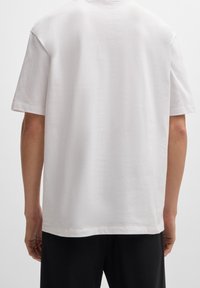 Biała bawełniana koszulka z krótkim rękawem o luźnym kroju, z klasycznym okrągłym dekoltem i minimalną liczbą szwów dla gładkiej tekstury.