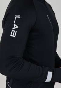 Schwarzes, athletisches Langarmoberteil mit weißem "ELITE LAB"-Branding auf dem Ärmel, das eine glatte Textur und ein elegantes Design aufweist.