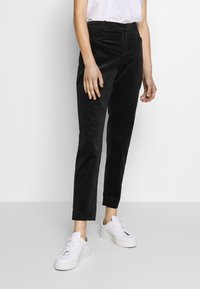 Svarta manchesterbyxor med slim fit, försedda med framfickor och hög midja, ihop med vita sneakers för en avslappnad look.