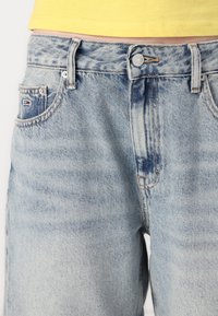 Lyseblå denim jeans med avslappet passform, som har fem lommer, synlige sømmer, og en liten flerfarget logo på frontlommen.