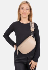 Beige Leder Crossbody-Tasche mit strukturiertem Finish und einem gemusterten Stoffgurt. Mit einem Reißverschlussverschluss und einer eleganten ovalen Form.