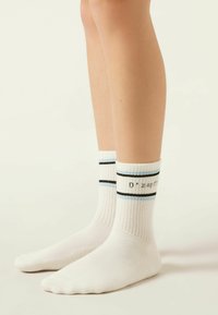 Weiße Knöchelsocken mit gerippter Textur, die blaue und schwarze Streifen am Bündchen sowie bedruckten Text auf einer Seite aufweisen.