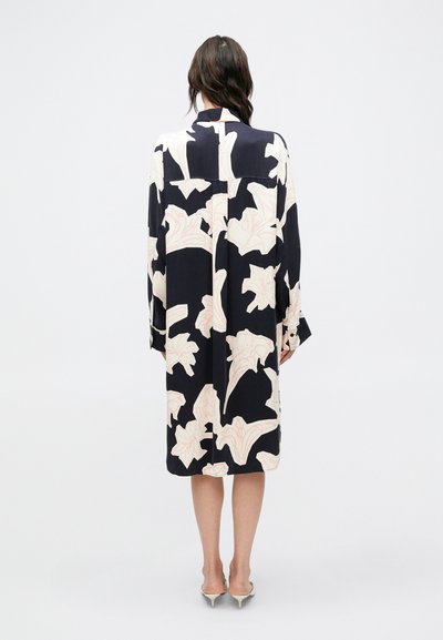 Αέρινο μαύρο φόρεμα με μεγάλα λευκά και ανοιχτό ροζ λουλουδένια μοτίβα, μακριά μανίκια και γιακά, με χαλαρή εφαρμογή και μήκος μέχρι τη μέση της γάμπας.