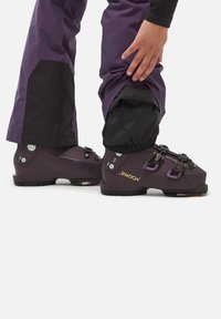 Bottes de ski en violet foncé avec des accents noirs. Comprend des boucles doubles, une tige texturée et une semelle robuste pour une adhérence sur la neige.