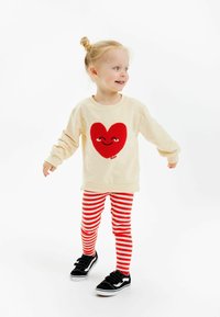 Beige sweatshirt med ett rödstickat hjärtdesign, matchad med röd och vit randig leggings och svarta sneakers med kardborreband.