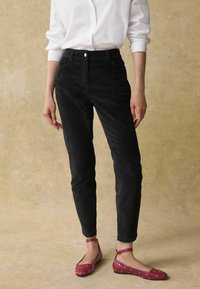 Pantalons en velours côtelé noir à taille haute et jambe droite, associés à des ballerines rouges à pois blancs. Fermeture à bouton simple.