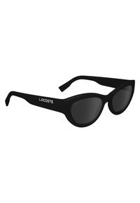 Black cat-eye sunglasses with dark lenses and matte finish, featuring a sleek design and white "LACOSTE" branding on the temples.