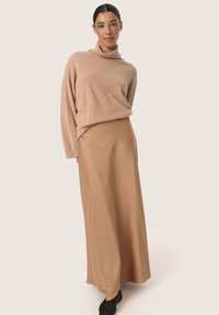 Beige sweater med rullekrave i blødt strikmateriale, kombineret med en glat, tanfarvet maxikjole. Oplægget har en afslappet pasform og høj talje.