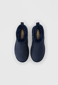 Ζευγάρι χειμερινές παντόφλες από σουέντ σε ναυτικό μπλε χρώμα με επένδυση από απαλό γούνα, φωτογραφημένες από πάνω σε απλό λευκό φόντο.