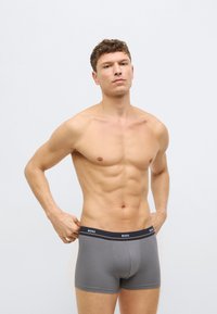 Szare bokserki z czarną elastyczną gumką w pasie z logo "BOSS". Gładka tkanina, dopasowany krój, długość do połowy uda, minimalna ilość szwów.