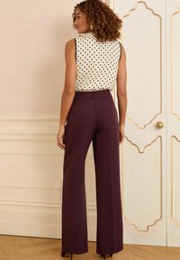Chemisier sans manches crème à pois noirs ; pantalon bourgogne taille haute à jambes larges ; texture lisse ; léger brillant ; associé à des talons.