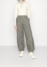 Pantaloni leggeri verde oliva con una vestibilità comoda, polsini elastici e tasche laterali, abbinati a un maglione di colore crema a coste e scarpe bianche chunky.