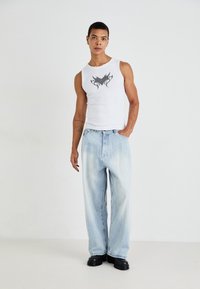 Hvit tanktopp med svart grafisk design, kombinert med lyseblå vide denimjeans og svarte platåsko.
