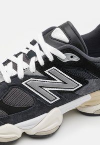 New Balance'i sussid, millel on must ja hall disain, võrgu pealis, nahast aktsendid, valged paelad, hõbedane logo ja tekstureeritud tallaosa.