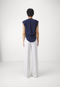 Blusa senza maniche blu navy con retro arricciato, abbinata a pantaloni bianchi a gamba larga. Tessuto morbido, vestibilità rilassata e leggera drappeggiatura.
