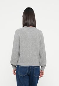 Suéter gris de punto con mangas largas, cuello redondeado y puños acanalados. Combinado con jeans de tiro alto azules, mostrando un ajuste informal.