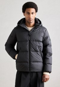 Doudoune noire en matière matelassée él�égante avec fermeture éclair, capuche ajustable et poches latérales. Bord-côtes texturé en tricot.