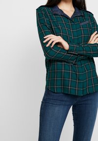 Grünes Karoshirt aus weichem Stoff mit einem Denim-Kragen und Schulterakzenten, mit geknöpften Manschetten und einer Brusttasche.