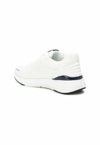 Zapatilla deportiva blanca con una parte superior de malla texturizada, una suela acolchada y un acento azul oscuro en el talón. Presenta un diseño de punta redondeada.