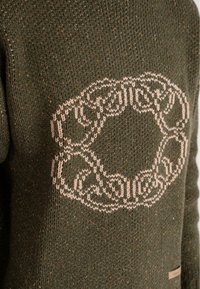 Green knitted sweater featuring a large, light beige circular pattern at the center, with a rough texture and speckled color detail throughout.