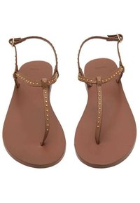 Sandali piatti marroni con design a T, decorati con piccoli chiodini dorati lungo le cinghie, realizzati in un materiale sintetico liscio.
