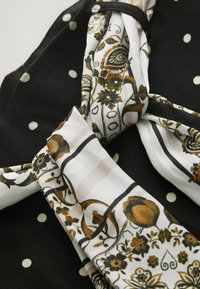 Tissu noué avec des sections noires et blanches ; les parties blanches présentent des motifs floraux et cachemire marron et noir, les parties noires ont des pois blancs.